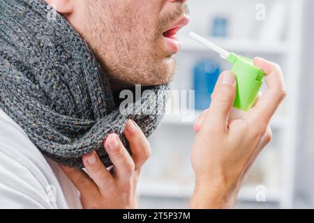 Nahaufnahme Mann mit grauem Schal um den Hals mit Spray gegen Halsschmerzen Stockfoto