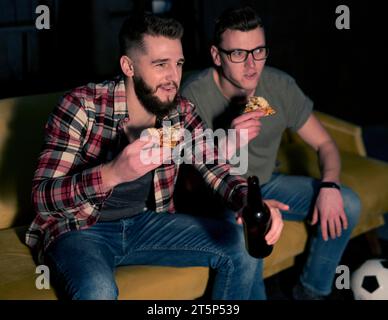 Männliche Freunde schauen zusammen Sport-tv, während sie Bier-Pizza trinken Stockfoto