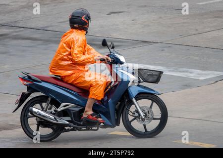 Ein Mann im Regenmantel fährt Motorrad auf der nassen Straße in Thailand. Stockfoto