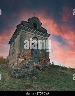 Mystisches Foto von der Ruine der Kapelle auf dem Hügel. Geheimnisvolle rosa-blaue Wolken hängen über dem Kreuz des Gebäudes Stockfoto