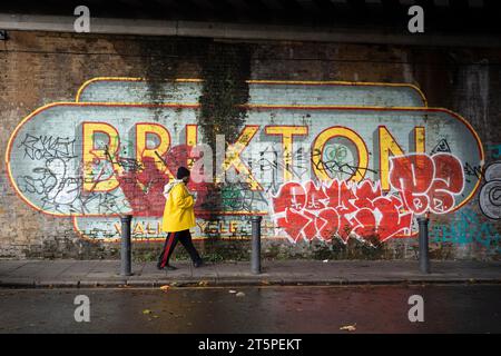 SüdLondoner laufen am 4. November 2023 unter einer Eisenbahnbrücke vorbei an einem großen Wandgemälde von Brixton in Brixton South London in London, England. Stockfoto