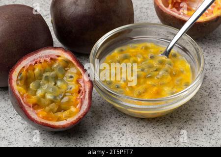 Halbierte frische tropische Passionsfrucht und eine Glasschale mit Passionsfruchtsaft und Samen aus nächster Nähe Stockfoto