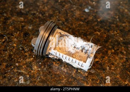 Ein verstopfter verschmutzter Filter aus der Waschmaschine wird entfernt und gereinigt, um die Verstopfung zu beheben. Stockfoto