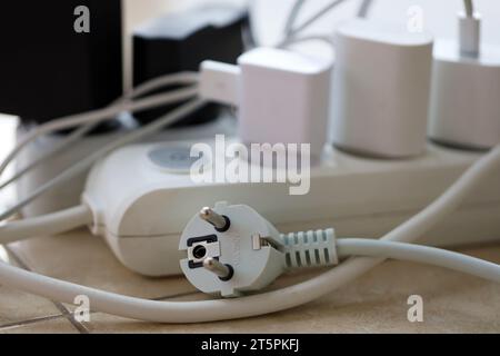 Überlastete Stromversorgungsplatinen. Steckdosenleisten mit verschiedenen Steckern auf weißem Boden. Konzept der Gefahr Gefahr Überlaststrom elektrisch Stockfoto