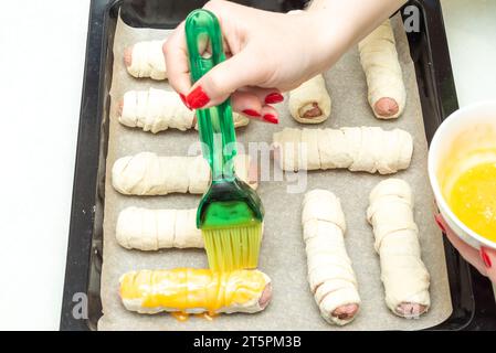 Würstchen vor dem Backen in rohem Teig mit Eigelb bestreichen. Zuhause Würstchen im Teig kochen. Stockfoto