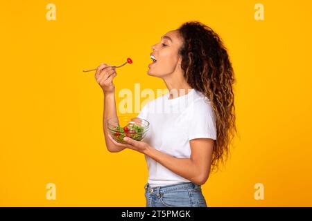 Junge schwarze Frau in zwangloser, genießt leckeren vegetarischen Salat, Studio Stockfoto