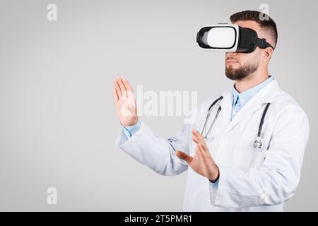 Doktor Mann mit Virtual-Reality-Headset, Interaktion auf grauem Hintergrund, freier Raum Stockfoto