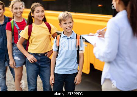 Schwarze Lehrerin, die Namen abfragt, während Kinder in den Schulbus steigen Stockfoto