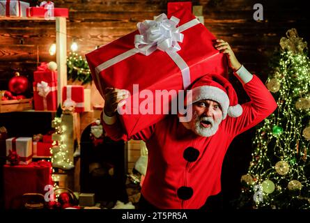 Frohe Weihnachten. Frohes Neues Jahr. Lieferservice. Überraschter Weihnachtsmann mit Weihnachtsgeschenk. Bärtiger Mann im weihnachtsmannkostüm mit großem Geschenk Stockfoto