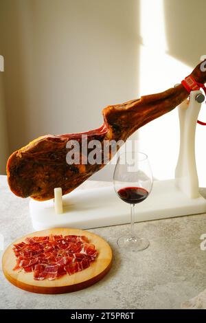 Spanische Jamón auf einem weißen Jamonera-Stand und Rotweinglas Stockfoto