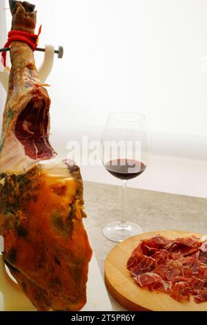 Spanische Jamón auf einem weißen Jamonera-Stand und Rotweinglas Stockfoto