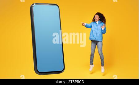 Die schwarze Dame springt und zeigt auf einen riesigen Bildschirm, Mockup Stockfoto