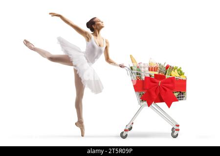 Balletttänzer in einem weißen Tutu-Kleid tanzt und schiebt einen Einkaufswagen mit roter Schleife isoliert auf weißem Hintergrund Stockfoto