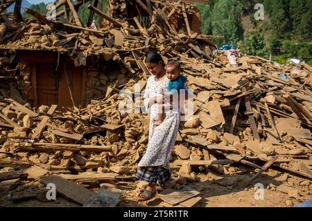 Jajarkot, Nepal. November 2023. Eine Frau mit einem Kind geht an einem Haus vorbei, das bei einem Erdbeben in Jajarkot, Nepal, am 6. November 2023 zerstört wurde. Insgesamt wurden am Montag um 19:00 Uhr Ortszeit 157 Tote und 349 weitere Verletzte bestätigt, und 17.529 Häuser wurden teilweise beschädigt und 17.792 weitere vollständig zerstört, so Nepals National Emergency Operation Center unter dem Ministerium für Inneres. Quelle: Sulav Shrestha/Xinhua/Alamy Live News Stockfoto