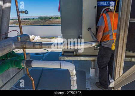 Ein neu geschweißtes Edelstahlrohr und ein Arbeiter, der in der Kompressorplatte eines CO2-Kühllagers (Industriekühlung) auf dem Dach arbeitet. Stockfoto