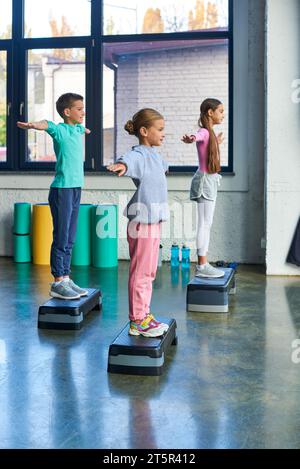 Drei Jugendliche Mädchen und Junge in Sportkleidung, die auf Fitness Stepper mit Armschichten trainieren, Sport Stockfoto