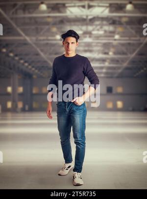 Junger Mann, der in einem großen, modernen, leeren Lagerhaus läuft, in die Kamera schaut, Ganzkörperaufnahme Stockfoto