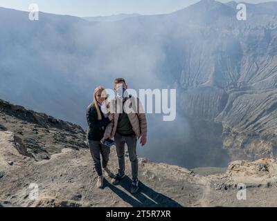 Junges Paar am Rand des aktiven Vulkankraters Bromo, Ost-Java, Indonesien. Panoramaansicht des Rauchgasdampfes aus dem Krater Stockfoto