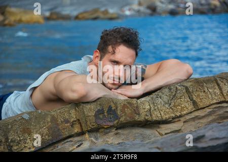 Ein Mann, der auf einem Felsen am Meer liegt. Foto eines Mannes, der sich an einem sonnigen Tag am Wasser entspannt Stockfoto