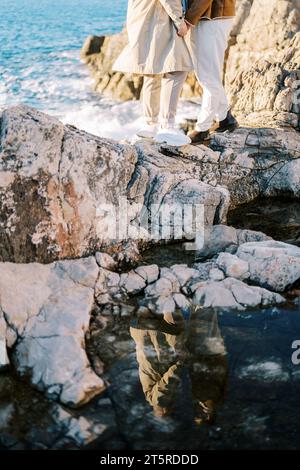 Zwei Männer stehen mit Händen auf einem Felsen über dem Meer Stockfoto