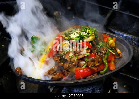 mexikanisches Essen, das Hühnchen und Rindfleisch-Fajitas auf heißem Brateller mit Feuer und Rauch raucht Stockfoto