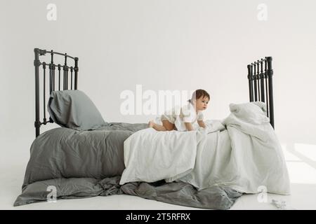 Porträt eines Kindes - ein Mädchen, das auf dem Bett kriecht und spielt. Kinderkonzept. Stockfoto