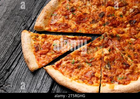 Pizza mit verschiedenen Fleischsorten, in Scheiben geschnitten, eine Scheibe wird auf schwarzem Holzhintergrund getrennt Stockfoto