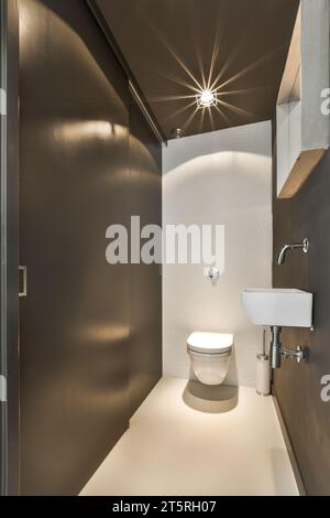 Ein Badezimmer mit Toilette, Waschbecken und Spiegel an der Wand in der rechten Ecke, von oben kommt ein Licht Stockfoto