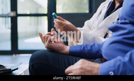 Alter Patient mit Glucometer-Instrument zur Diabeteskontrolle, Spezialist zur Messung des Glukosezuckerspiegels im Insulintest. Arzt überprüft Blutprobe für diabetischen Seniorenmann im Krankenhausbereich. Stockfoto