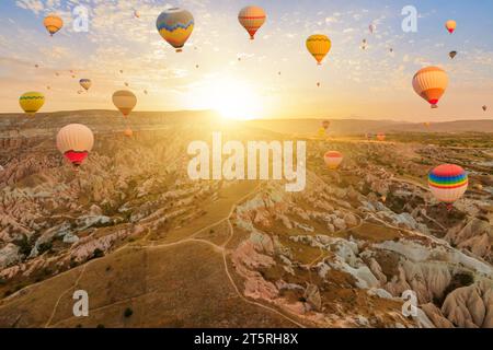 Ballons steigen am Himmel von Kappadokien auf. Die strahlenden Ballons erfassen das sinkende Sonnenlicht und werfen ein mystisches Licht auf die surrealen Gipfel darunter Stockfoto