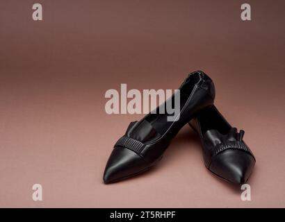 Klassische schwarze, spitz zulaufende Lederballet-Ballerinas mit Faltendetails und Rüschen auf braunem Hintergrund. Kopierbereich. Das Konzept des modernen foo Stockfoto