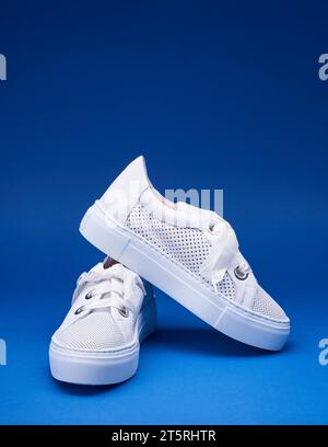 Trendige weiße Sneakers aus perforiertem Leder mit dicken, genähten Gummisohlen auf dem verlaufsblauen Hintergrund mit Kopierraum. Urbaner STYLE, Schuhverkauf Stockfoto