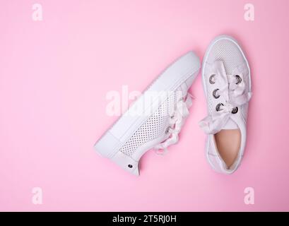Blick von oben auf stilvolle weiße, legere Sneakers aus perforiertem Leder auf weichem rosa Hintergrund mit Kopierraum. Modischer, stylischer Sportschuh Stockfoto