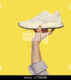 Ein stilvoller weißer Sneaker in der Hand eines kaukasischen Mannes, isoliert auf gelbem Hintergrund. Konzept der Werbung für Sportschuhe. Poster für das Outlet-Marketing. Mini Stockfoto