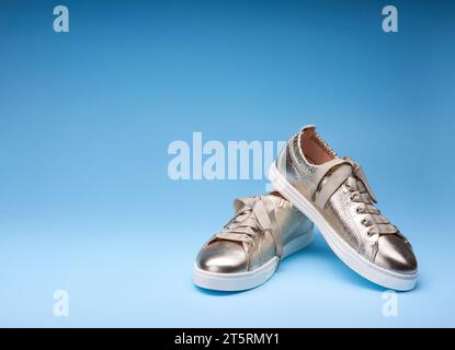 Moderne Sneakers aus goldfarbenem Metallic-Leder auf einem blau verlaufenden Hintergrund. Kopierbereich oben und links. Kreatives minimalistisches Layout mit Schuhen Stockfoto