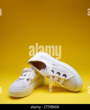 Trendige weiße Sneakers aus perforiertem Leder mit dicken Gummisohlen, isoliert auf einem verlaufsgelben Hintergrund mit Kopierraum. Modefotografie Stockfoto