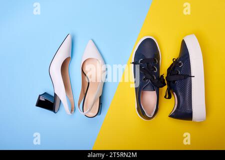 Eine Nahaufnahme von zwei Paar modernen Damenschuhen: Offene weiße Pumps mit schwarzen Absatzschuhen und lässige marineblaue Sneakers auf einem blau-gelben B Stockfoto