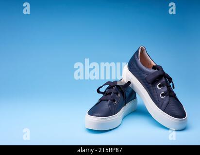 Trendige marineblaue Sneakers auf dem verlaufsblauen Hintergrund. Perforiertes Leder, Metallösen, dicker Schnürsenkel, weiße Gummisohle. Stilvoller Mini Stockfoto