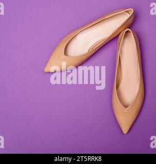 Moderne beige flache Damenschuhe mit spitzer Spitze auf einem hellen lila Hintergrund. Draufsicht. Modefotografie Stockfoto