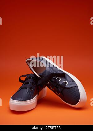 Stilvolle, legere, marineblaue Sneakers mit dicken weißen Sohlen und breiten Schnürsenkeln, isoliert auf einem leuchtend rot-orangen Hintergrund mit Kopierraum für Text. Adve Stockfoto