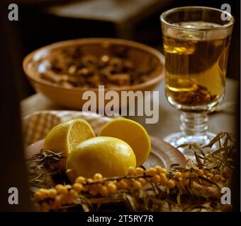 Zitronen und Sanddornzweige auf einer karierten Tischdecke. Ein Glas heißen Sanddorntee ist dahinter. Warme Herbstgetränke. Gesundheitsbegriff Stockfoto