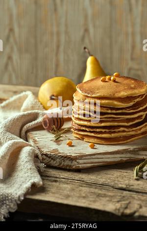 Ein Stapel Haferflockenpfannkuchen auf einem hellen Holztisch, umgeben von einem Paar Birnen in der Ferne, Sanddornbeeren und einem Löffel für pou Stockfoto