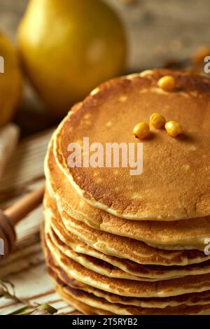 Flauschige hausgemachte Pfannkuchen auf einem hellen Holzbrett, mit Birnen und einem Löffel für Honig im Hintergrund. Das Konzept eines festlichen Abendessens. Food-Blog. Serv Stockfoto