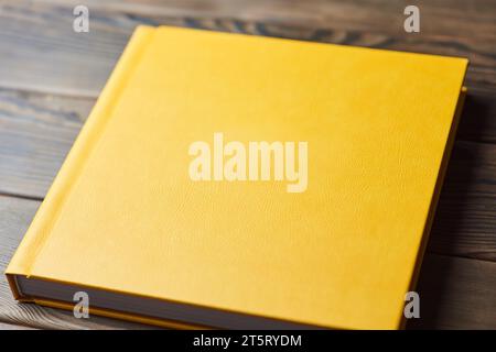 Stilvolles Buch mit gelbem Hardcover aus Leder, isoliert auf hölzernem Hintergrund. Perspektivische Ansicht, Nahaufnahme. Fotobuch, Fotoalbum, Tagebuch, Planer oder Schrott Stockfoto