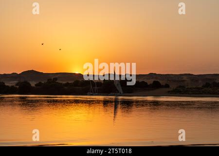 Die Sonne untergeht hinter Segelbooten und den Sandsteinhügeln am Ufer des Nils Stockfoto
