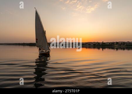 Felucca traditionelles ägyptisches Segelboot fährt bei Sonnenuntergang auf dem Nil den Fluss hinunter Stockfoto