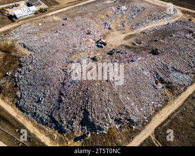 Aus der Vogelperspektive auf einer riesigen Deponie, wo Bulldozer arbeiten und LKWs neue Abfälle bringen. Riesige Vogelschwärme fliegen über die Szene. Stockfoto