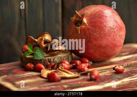 Reifer Granatapfel, Hagebuttenbeeren, getrocknete Äpfel und Minzblätter auf einer Holzoberfläche. Zutaten für die Zubereitung von gesundem Herbsttee. Stillleben. Stockfoto