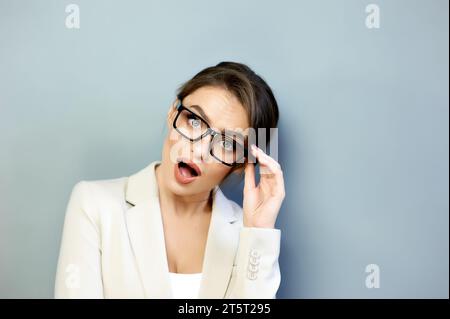 Porträt einer erstaunten jungen Frau, die eine stilvolle schwarz gerahmte Brille trägt, isoliert auf grauem Hintergrund mit Kopierraum. Beeindruckt vom Erfolg von t Stockfoto