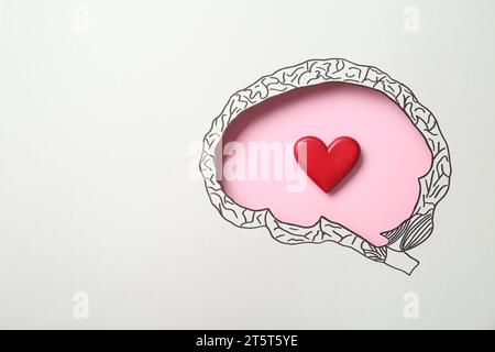 Emotionales Denken. Rotes Herz auf rosa Hintergrund, Draufsicht durch Papier mit hirnförmigem Loch und Zeichnung. Leerzeichen für Text Stockfoto